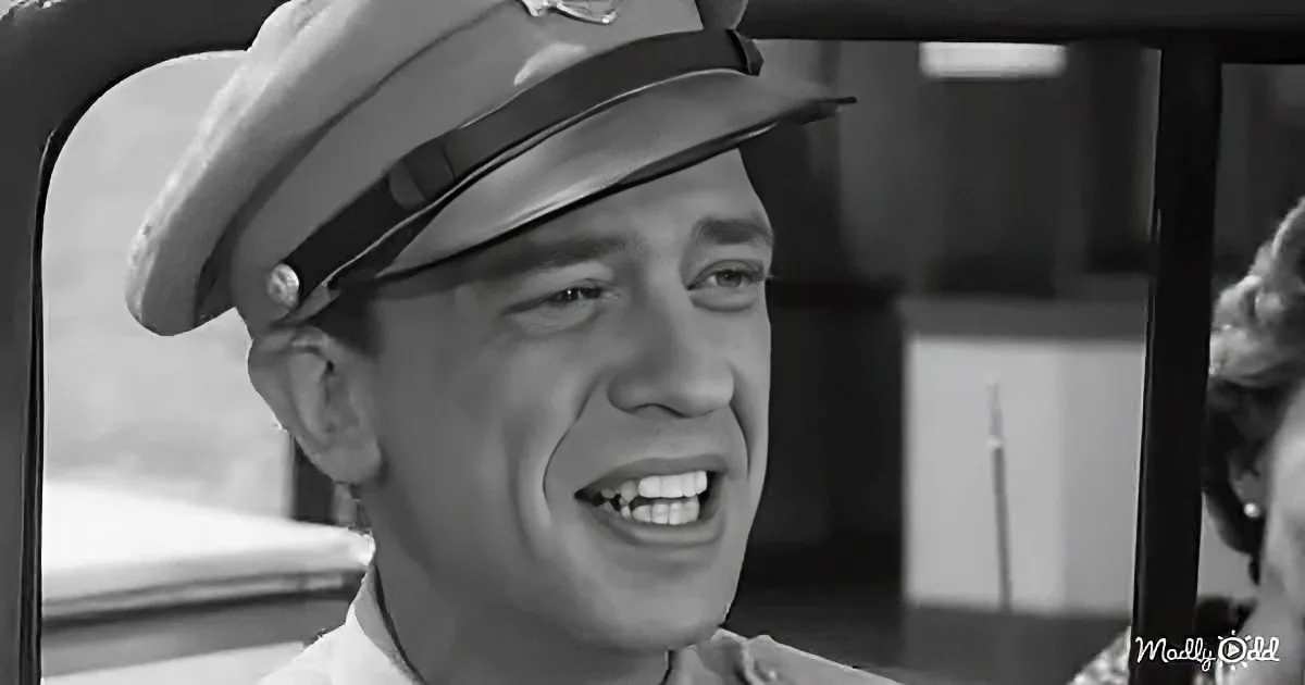 A man in a police uniform and hat is smiling, looking to the side, with a black-and-white background.