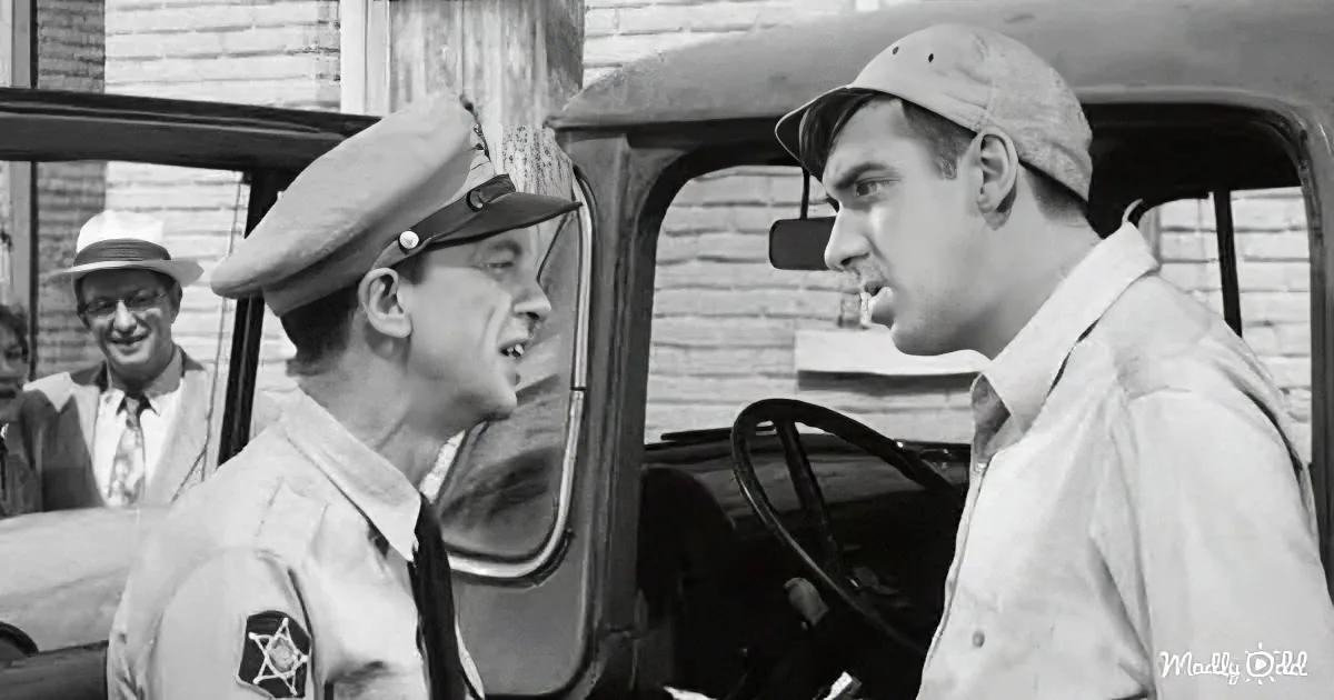 A sheriff in uniform talks to a man in a hat, both near a vintage car, with a curious onlooker in the background.
