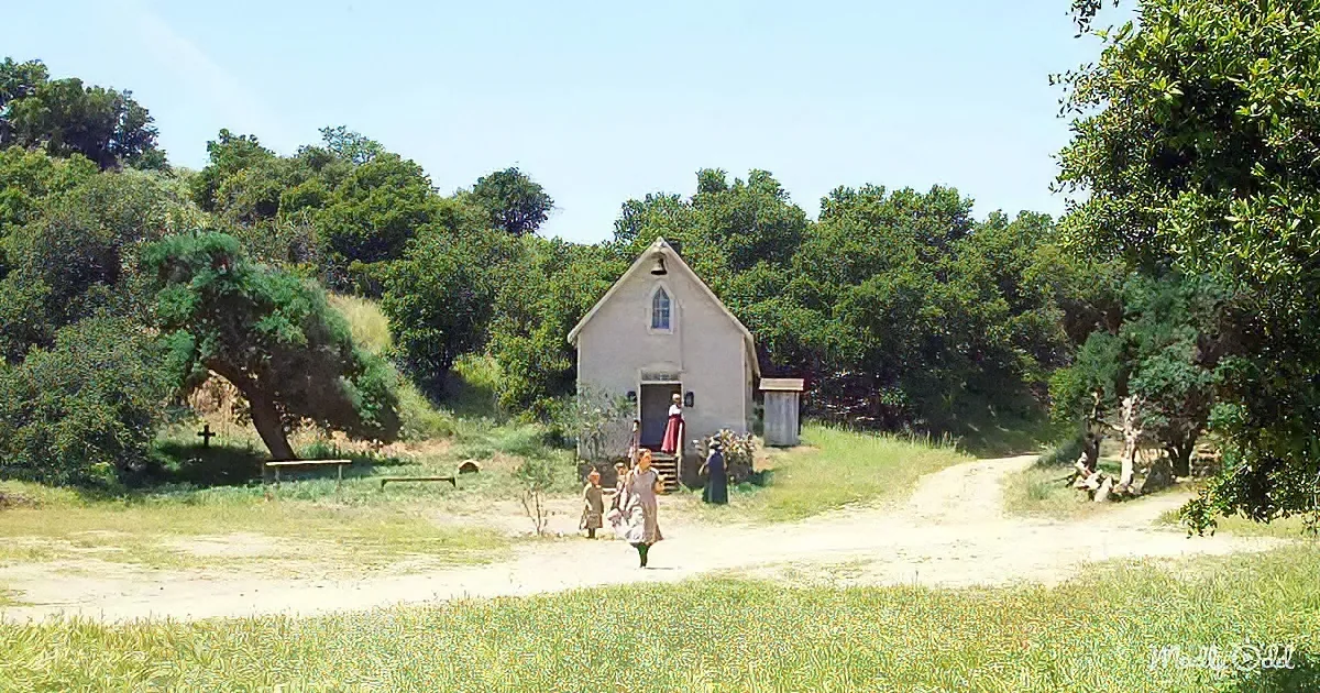 A small white church with people exiting, surrounded by lush green trees and a dirt path.