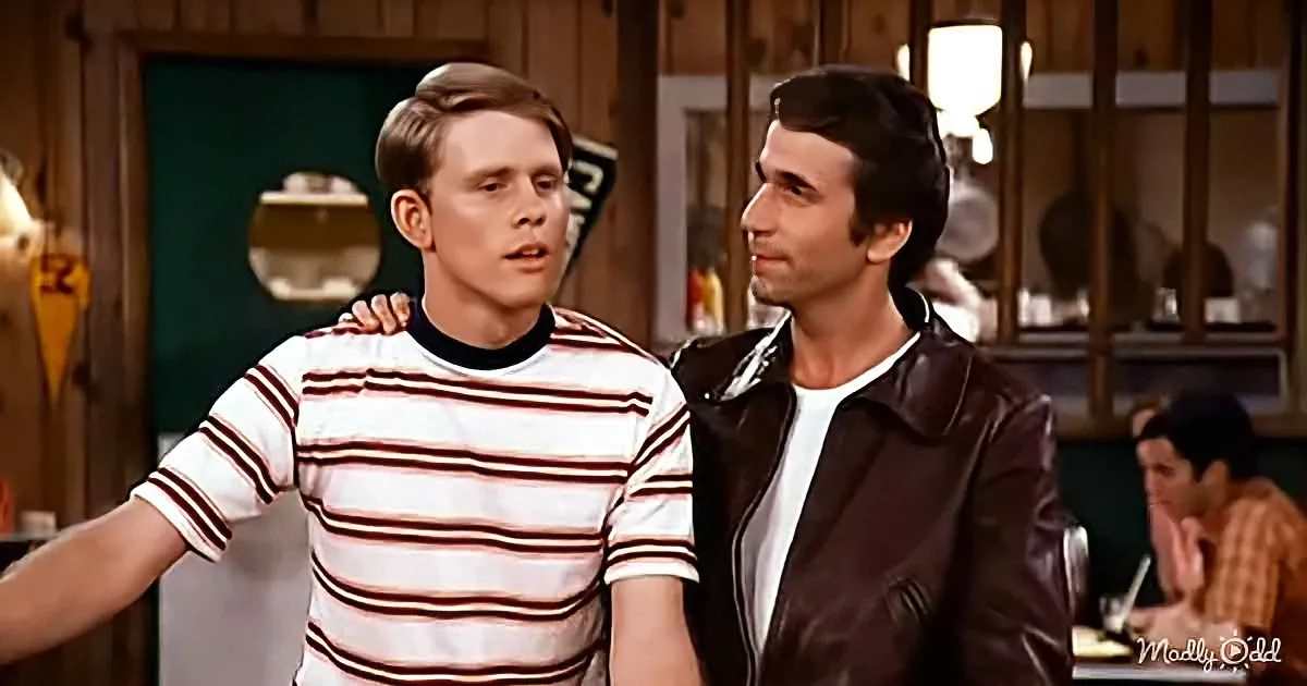Two men stand close, one in a striped shirt, the other in a leather jacket, in a diner setting.
