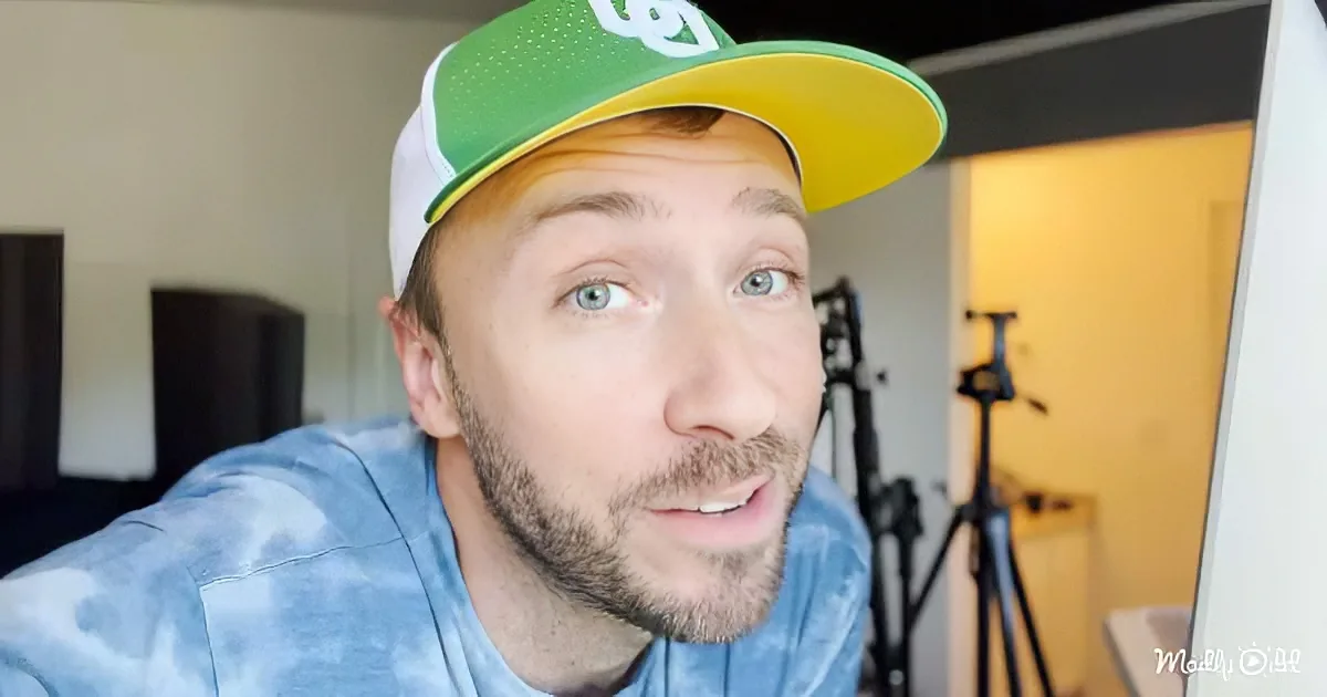 A person wearing a green and yellow cap and a blue tie-dye shirt is looking up, with a tripod and camera visible in the...