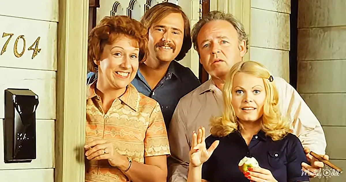 A family of four stands in front of a door numbered 704, smiling and waving.