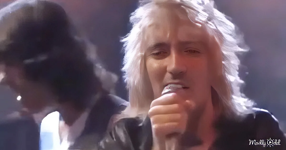 A person with long white hair sings into a microphone, with another person in the background.
