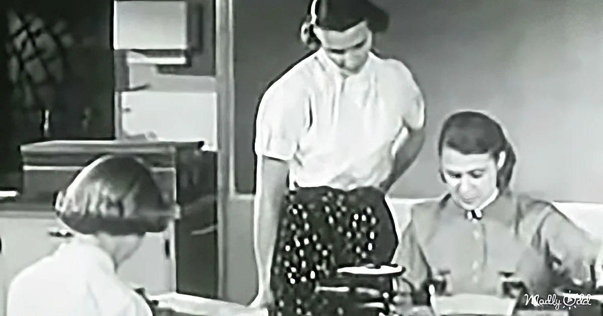 A person in a white shirt stands behind a typewriter, while another person sits at a desk, both wearing headsets.