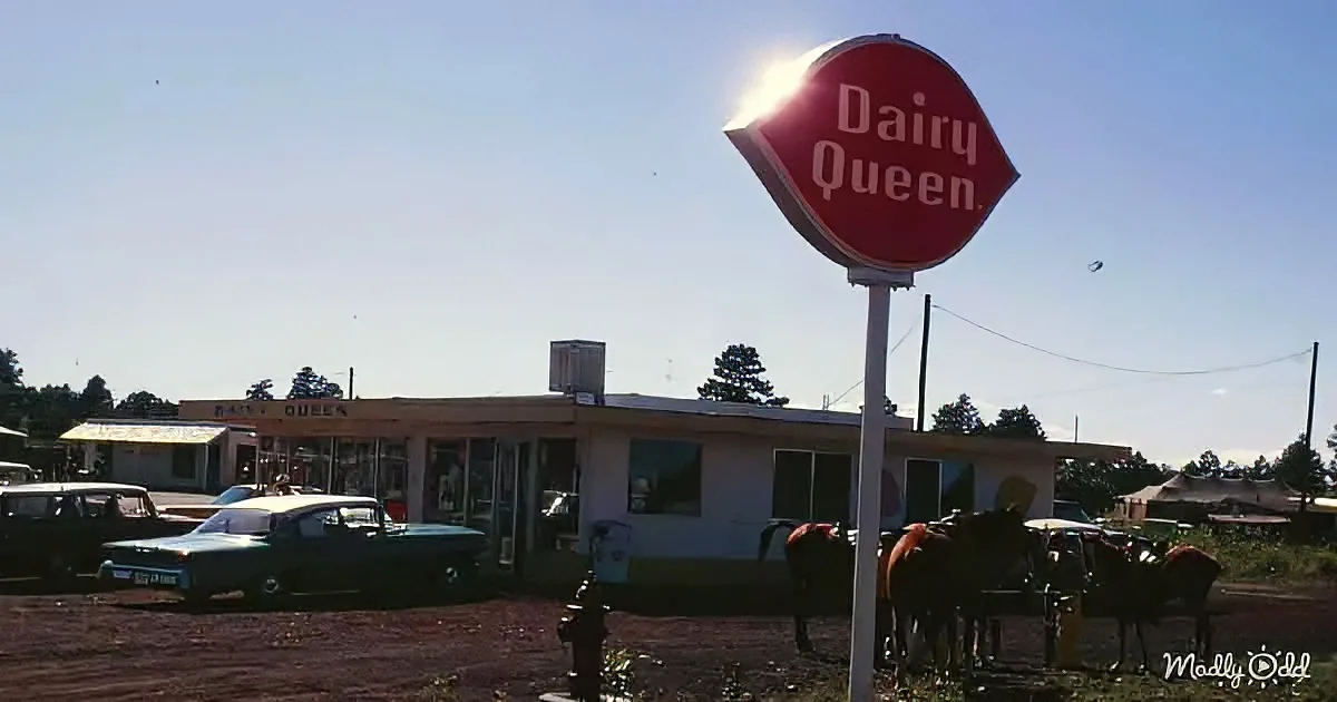 A Dairy Queen sign stands prominently in front of a vintage building with classic cars and horses nearby.