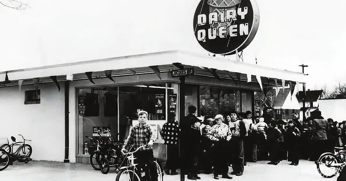 People queue outside a Dairy Queen ice cream shop with bicycles parked nearby.