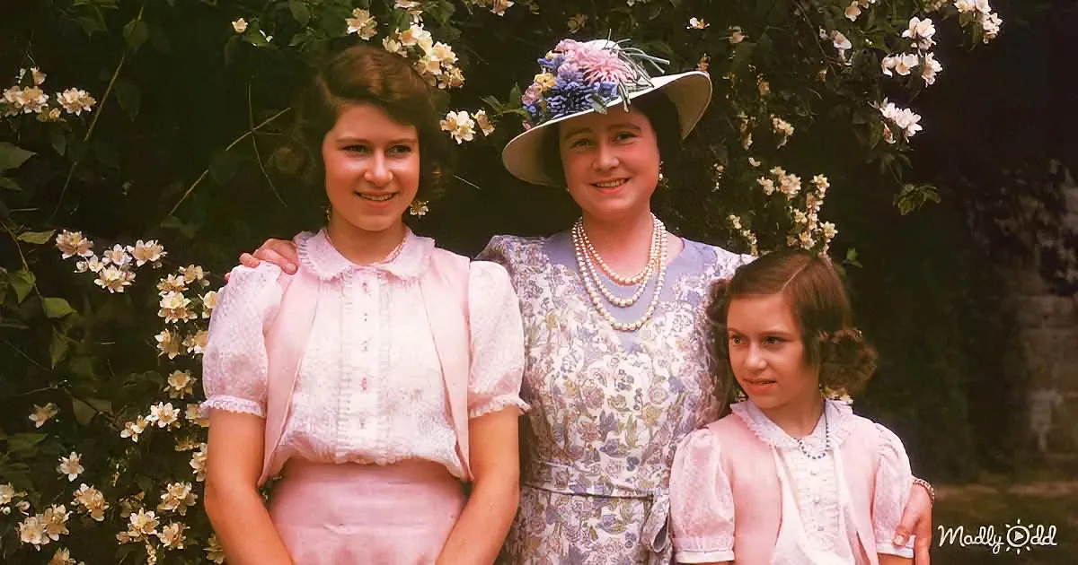 A woman in a floral dress and hat stands with two young girls in pink dresses, surrounded by white flowers.