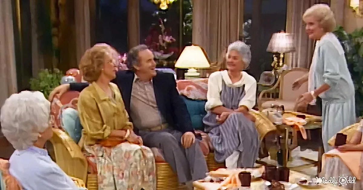 A woman in a blue dress stands while others sit in a cozy living room, engaged in conversation.