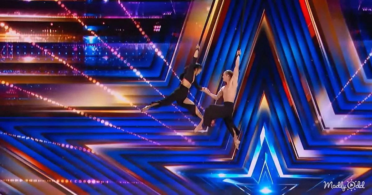 Two dancers perform acrobatics on a brightly lit stage with geometric patterns.