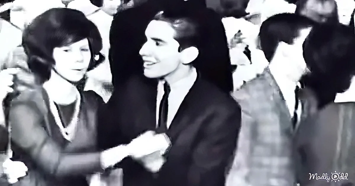A man and woman are dancing closely, surrounded by a crowd in a lively setting.