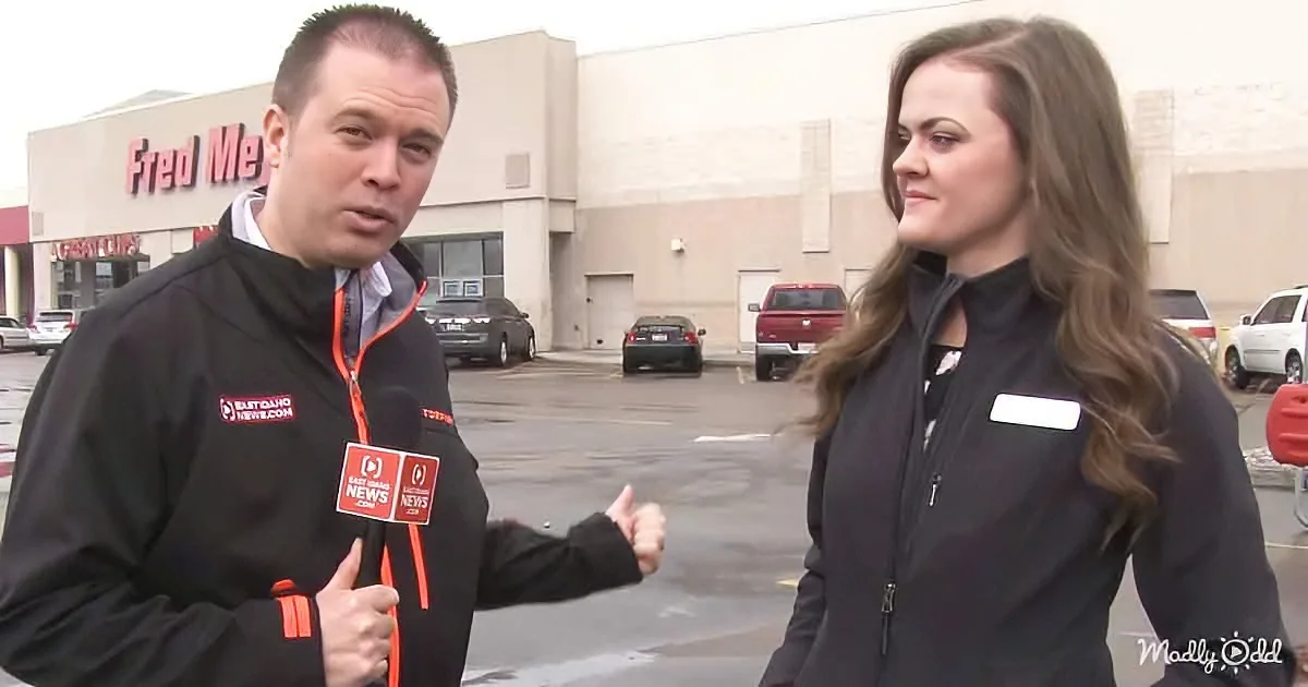 A man in a black jacket holds a microphone, interviewing a woman in a black jacket outside a Fred Meyer store.