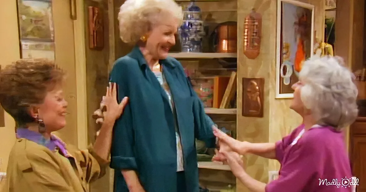 Three women in a kitchen, one in a teal shirt smiling, another in a purple shirt reaching out, third in a brown jacket...