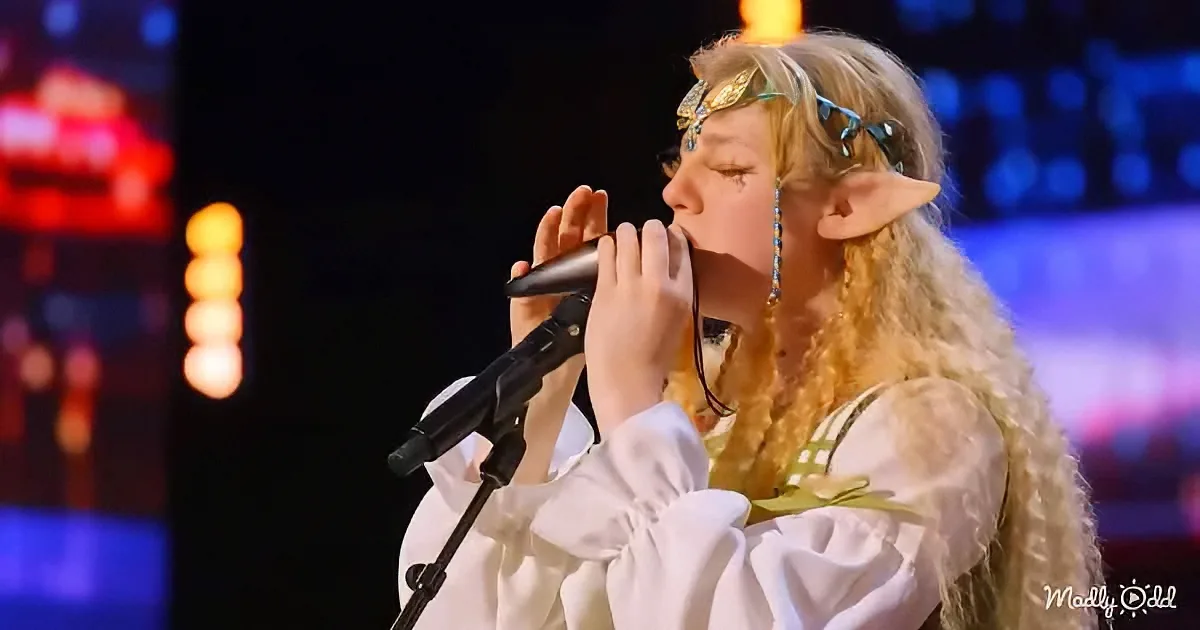 A person in an elf costume sings into a microphone on stage with colorful lights.
