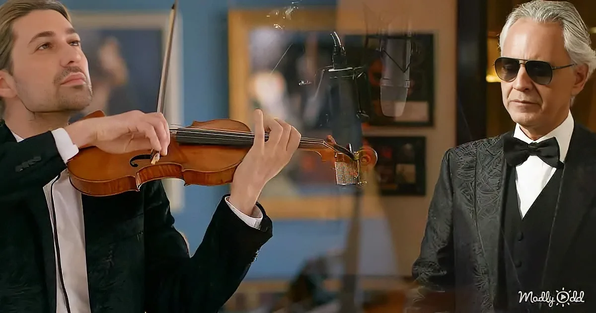 A man in a suit plays a violin while another man in sunglasses watches attentively.