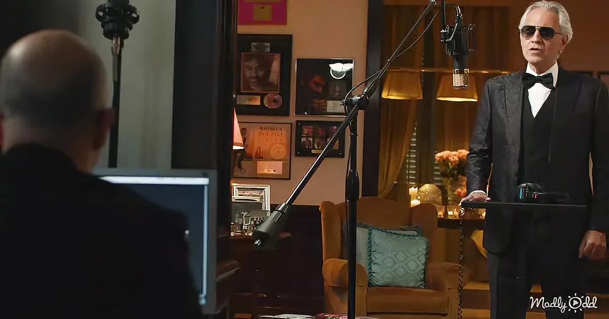 A man in a tuxedo stands in a recording studio, facing another man seated at a desk with a computer.