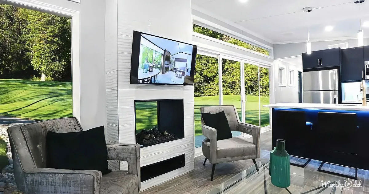 A modern living room with a fireplace, TV, and large windows overlooking a green lawn.