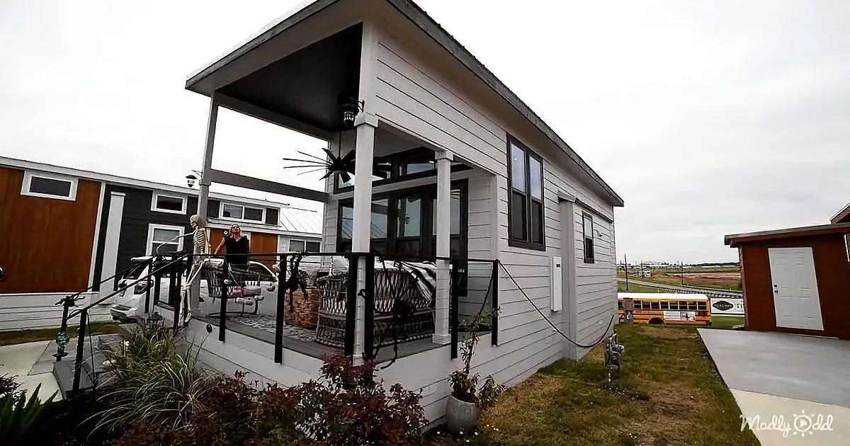 A white modern house with a covered porch, black railings, and a small garden in front.