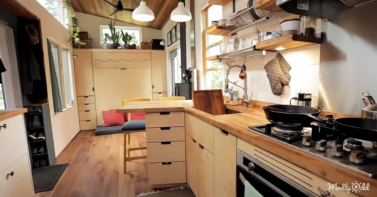 A cozy, compact kitchen with wooden cabinets, a gas stove, and a small dining area with a bench and cushions.