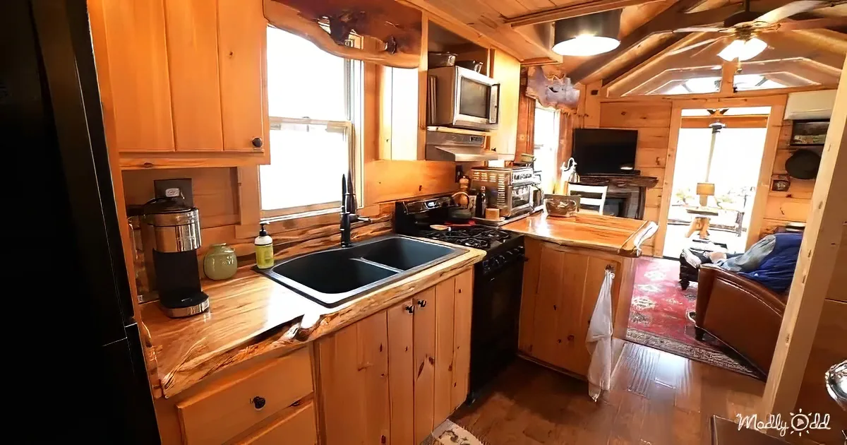 A cozy cabin kitchen with wooden cabinets, a sink, stove, and a view of a living area with a couch and TV.