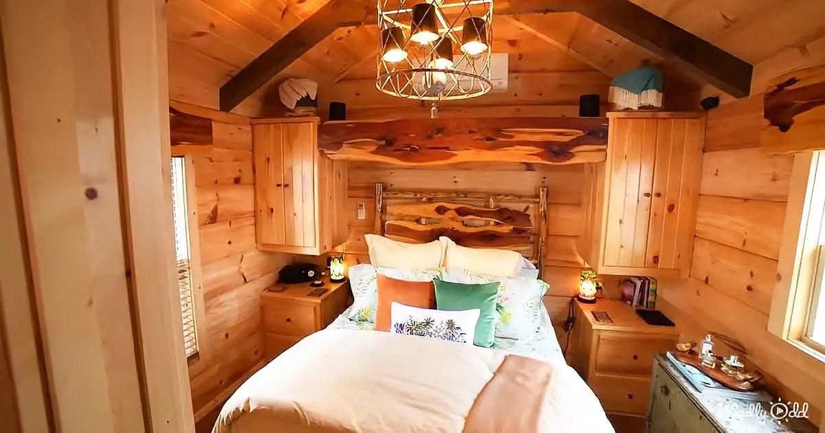 A cozy wooden cabin bedroom with a bed, wooden walls, and a chandelier.