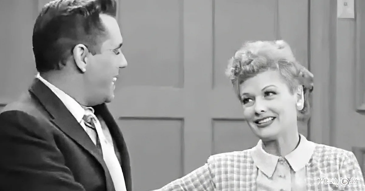 A man in a suit and a woman in a checkered dress are smiling and looking at each other.