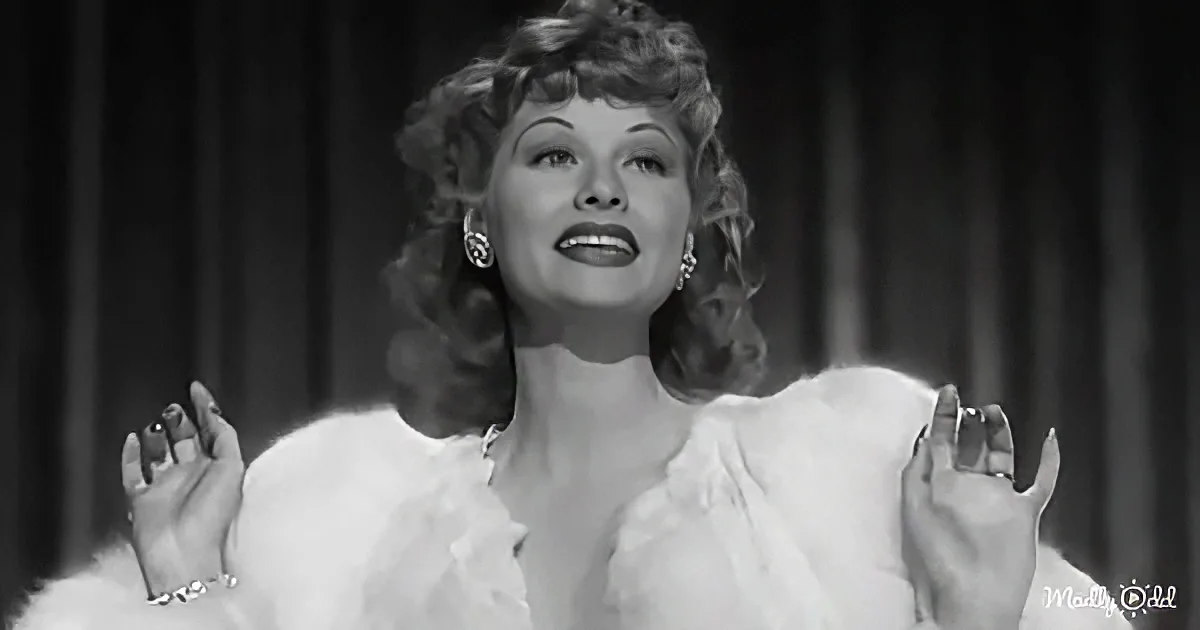 A woman in a white fur coat and elegant attire is posing with her hands raised, wearing pearl earrings and a ring.