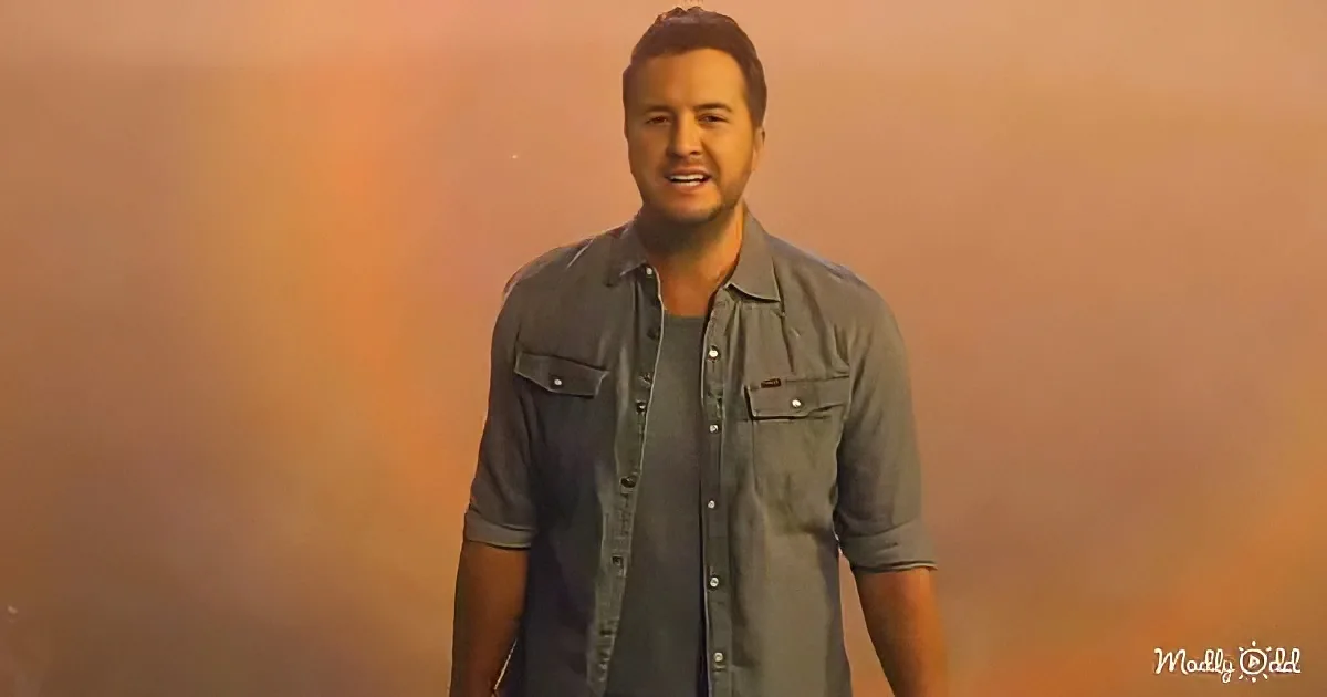 A man in a gray button-up shirt stands against a gradient background, smiling.