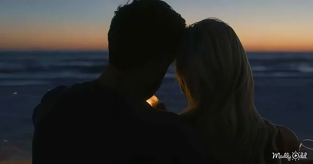 A silhouette of a couple embracing against a sunset backdrop by the sea.