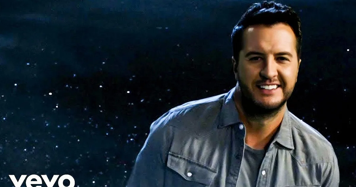 A smiling man in a denim shirt stands against a starry background.