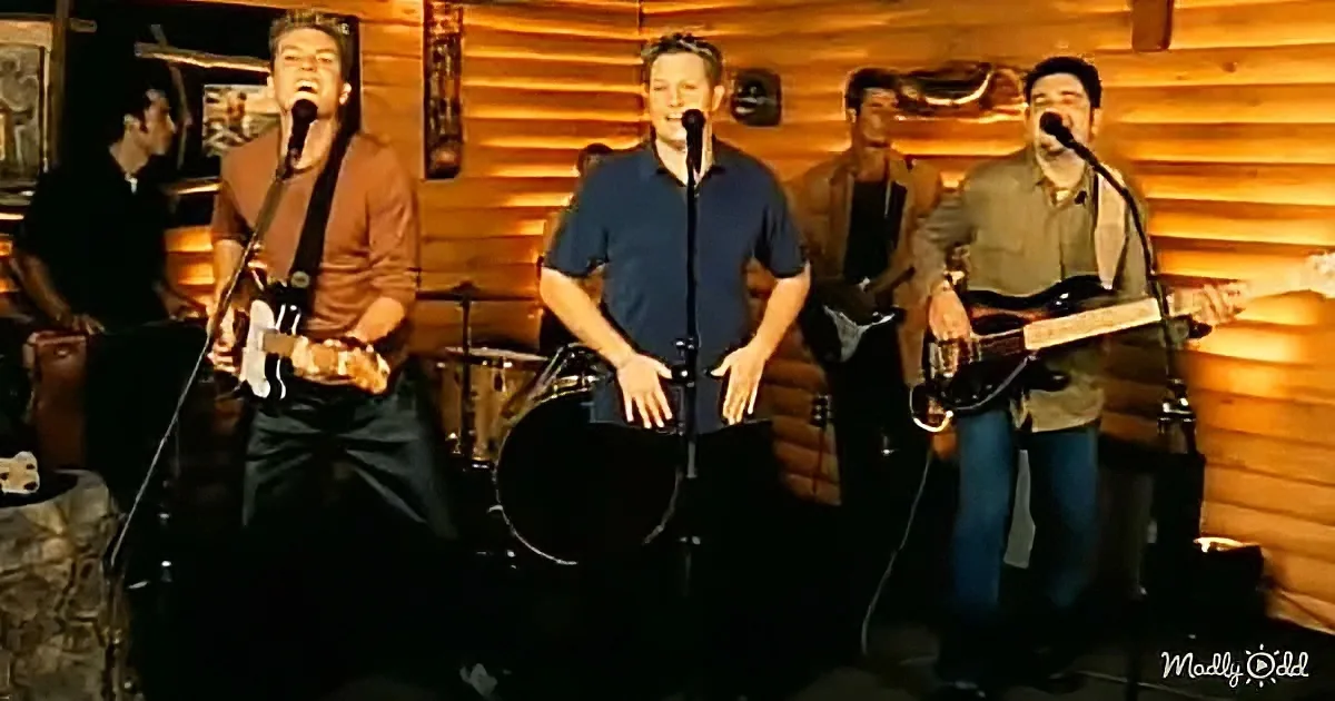 A band performs on stage with microphones, guitars, and a drummer in a wooden cabin setting.