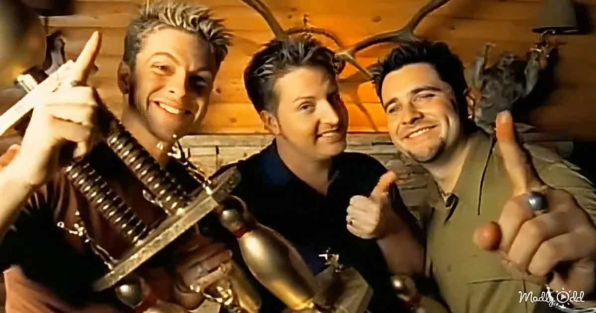Three individuals in a rustic setting, one holding a large gun, all giving thumbs up.