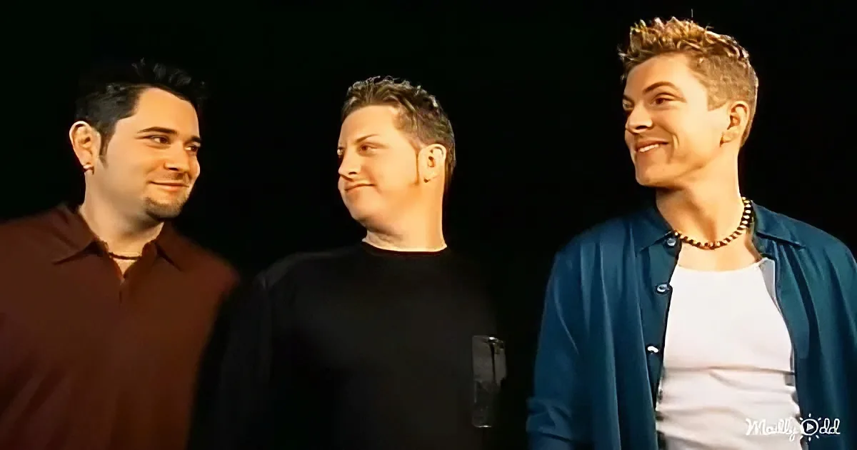 Three men in casual attire smile and pose together against a dark background.