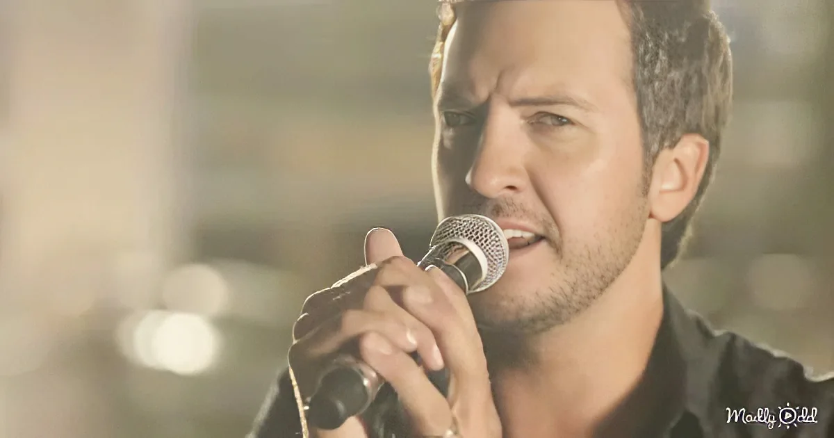 A man with short brown hair holds a microphone close to his mouth, singing.
