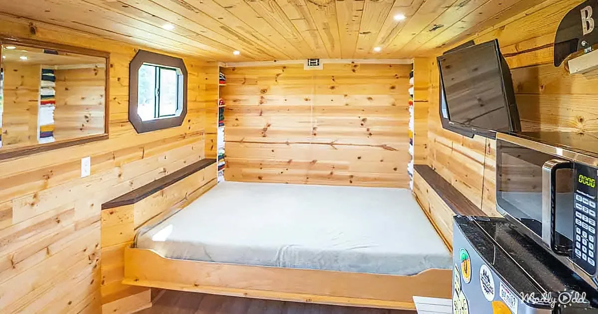 A cozy cabin interior with wooden walls, a bed, a microwave, and a small window.
