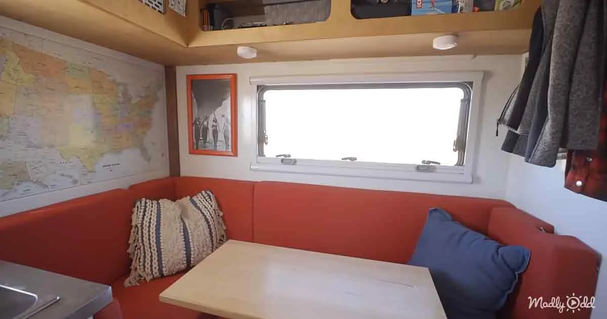 A cozy, compact living space with a red sofa, wooden table, map on wall, framed picture, and window.