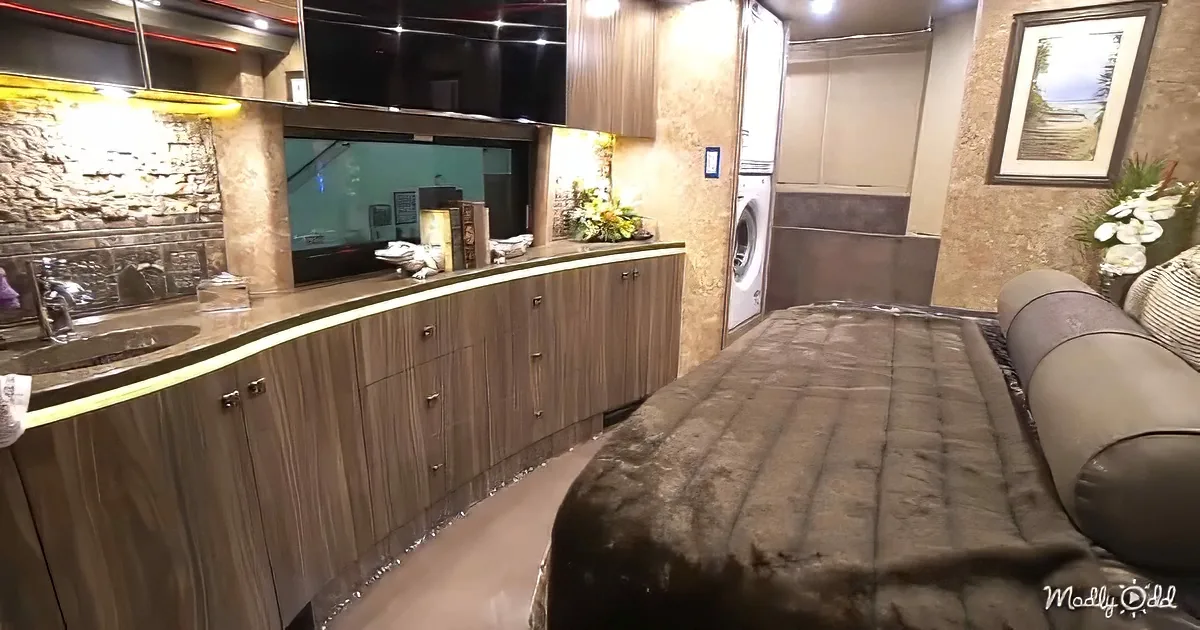 A luxurious RV interior with a bed, kitchen counter, sink, cabinets, and a washer/dryer.