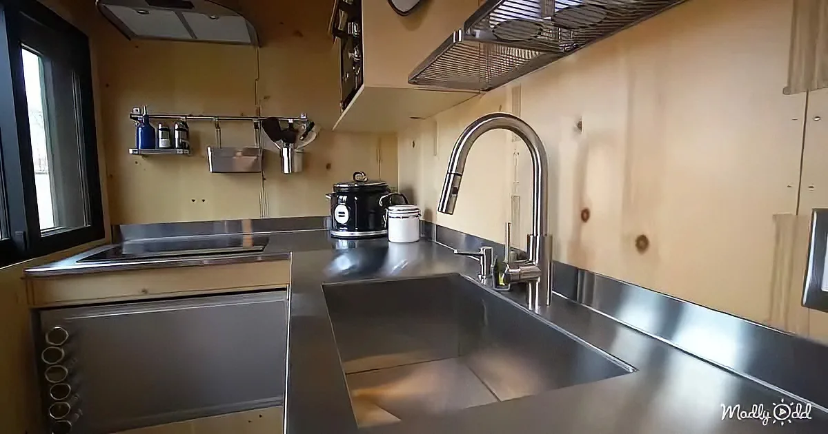 A compact kitchen with stainless steel sink, microwave, and wooden walls.