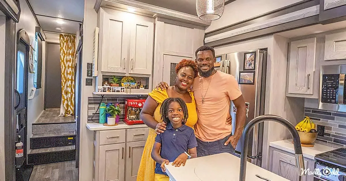A family of three stands together in a modern kitchen, smiling and embracing.