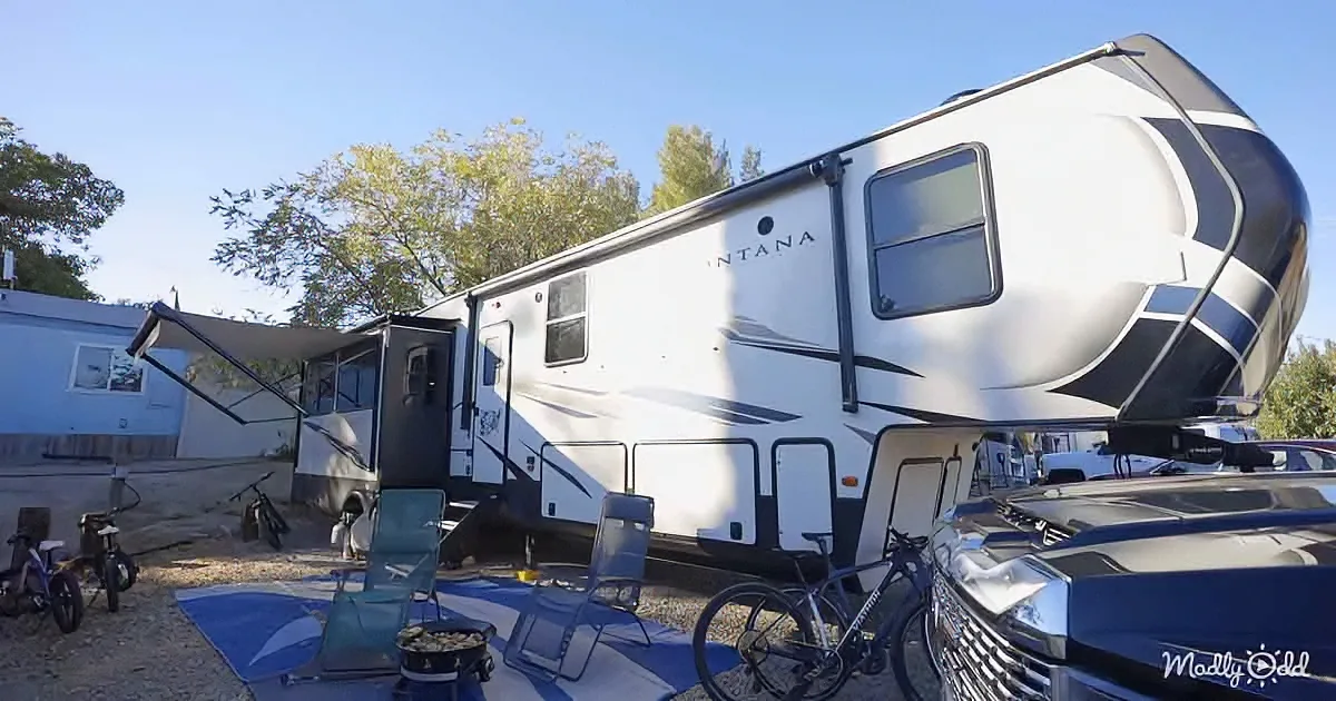 A Montana fifth-wheel RV is parked with a bicycle, chairs, and a blue blanket nearby, under a clear sky.