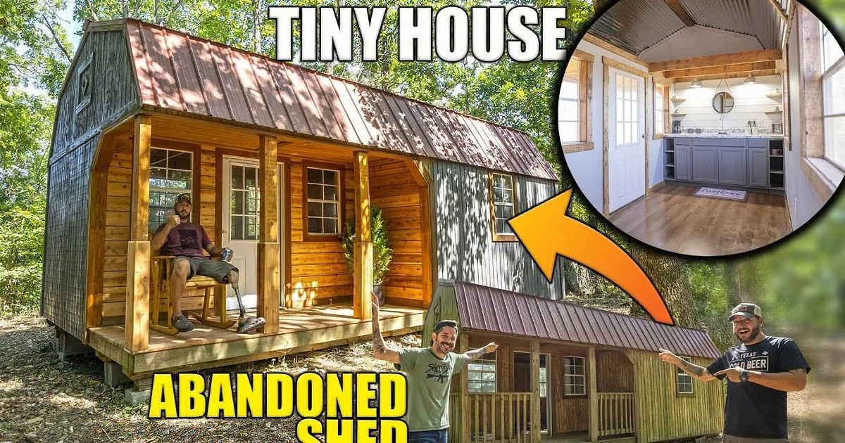 A man paints a dark green cabin with a wooden porch in a forested area.