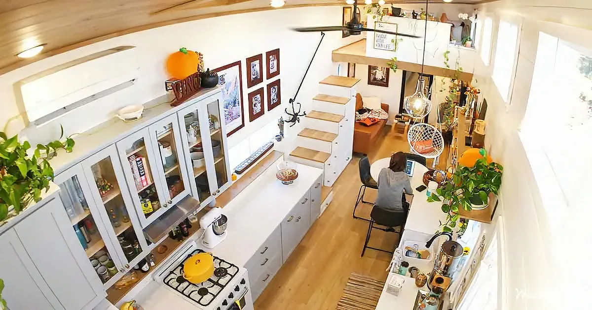A cozy, well-lit kitchen with white cabinets, a yellow pot on the stove, and a person sitting at a table.