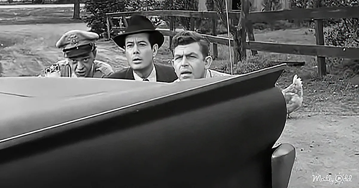 Three men peer from behind a car, appearing surprised or concerned, with a chicken in the background.