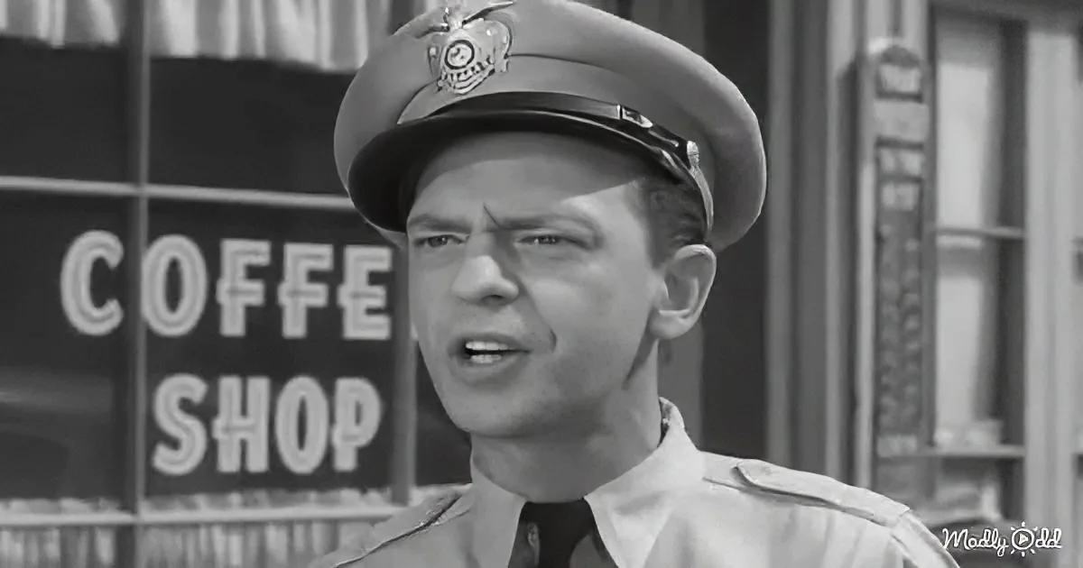 A man in a police uniform stands in front of a coffee shop sign, looking to the side with a serious expression.
