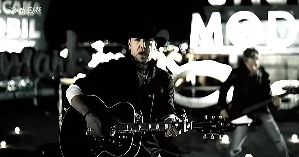 A man in a black outfit plays an acoustic guitar on stage with a band.