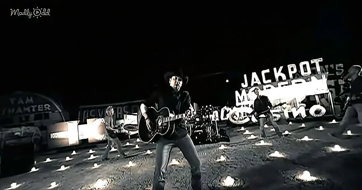 A man in a cowboy hat plays guitar in front of a "Jackpot" sign at night.