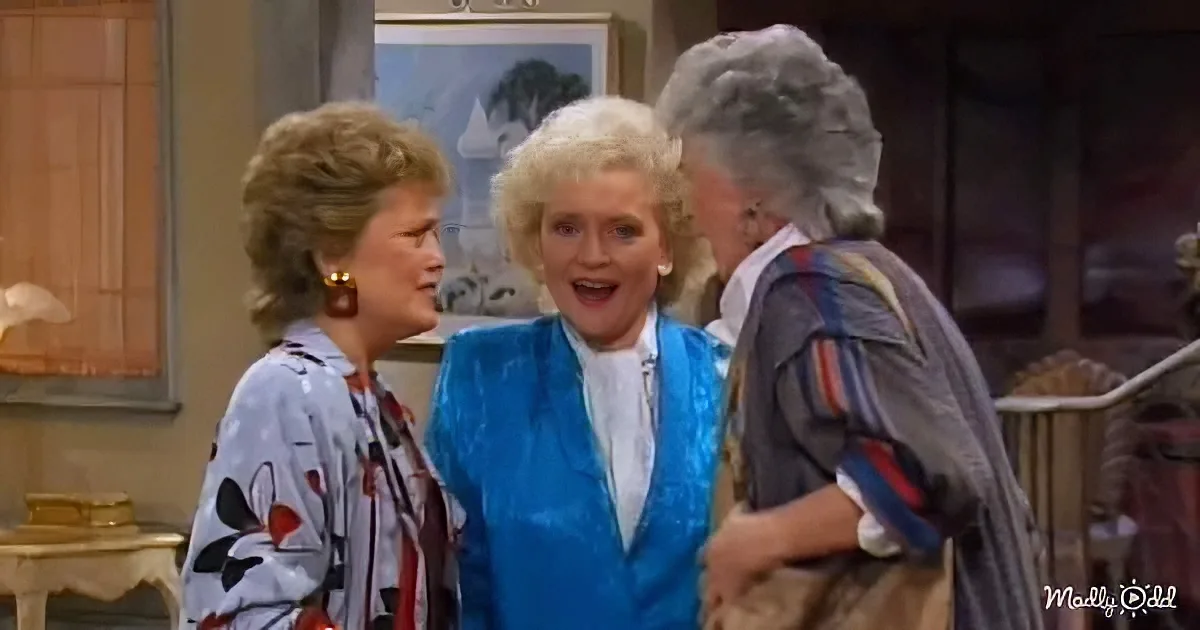 Three women in a room, one in blue jacket appears surprised, another in patterned shirt looks concerned, third in striped...