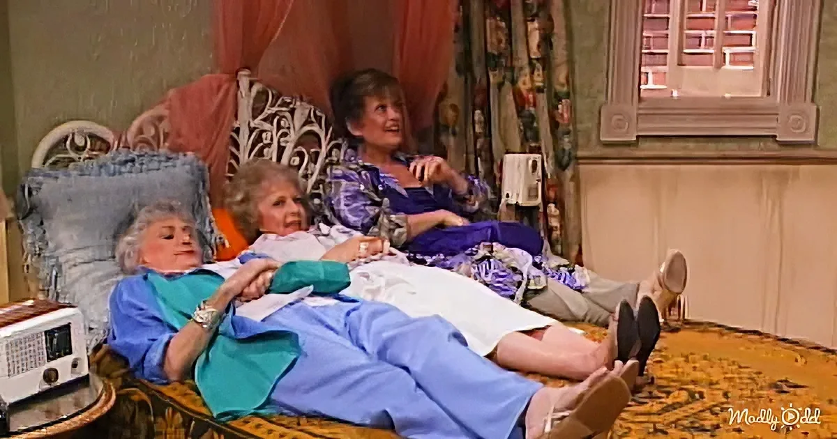 Two women in a cozy living room, one reclining on a chair, the other lying on a couch, both appearing relaxed and engaged...