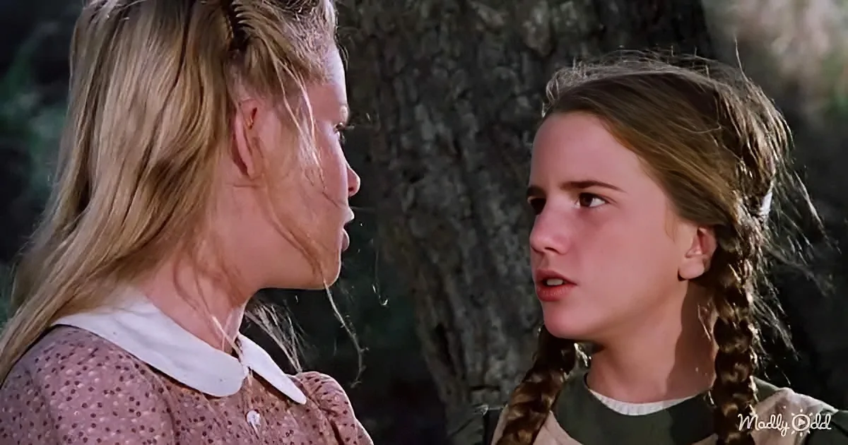 Two women, one with braids, appear to be having a serious conversation in a wooded setting.