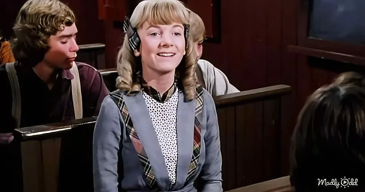 A young woman with blonde hair in pigtails smiles in a classroom setting, wearing a plaid vest over a polka-dot shirt.