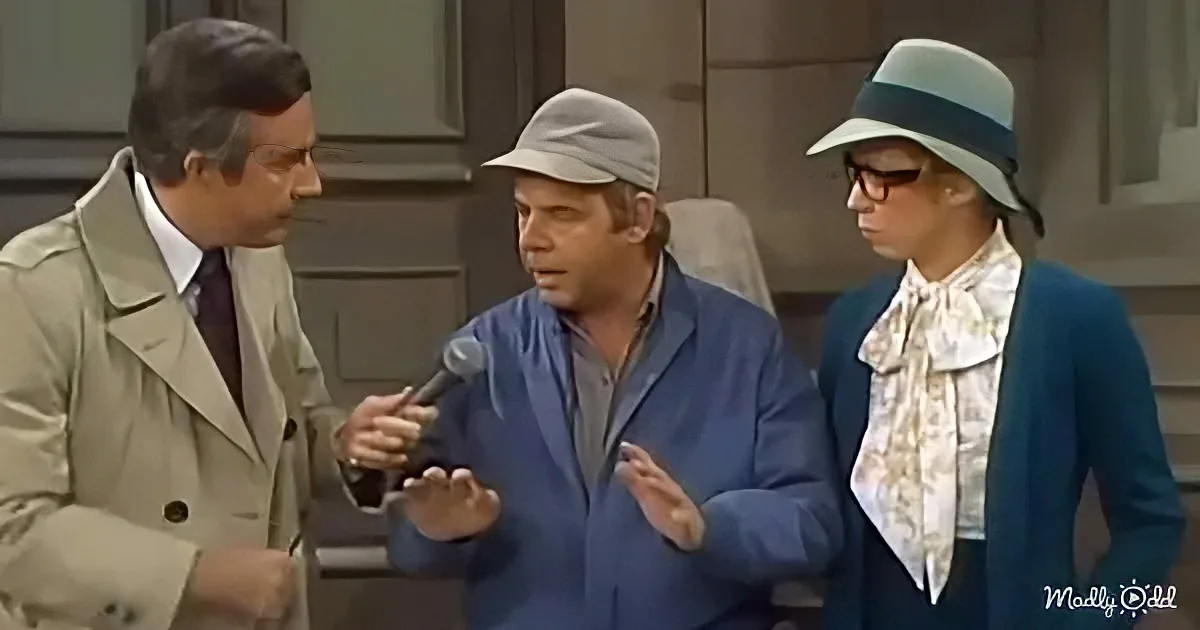 A man in a trench coat holds a microphone, interviewing another man in a blue suit and hat, with a woman in a blue coat...